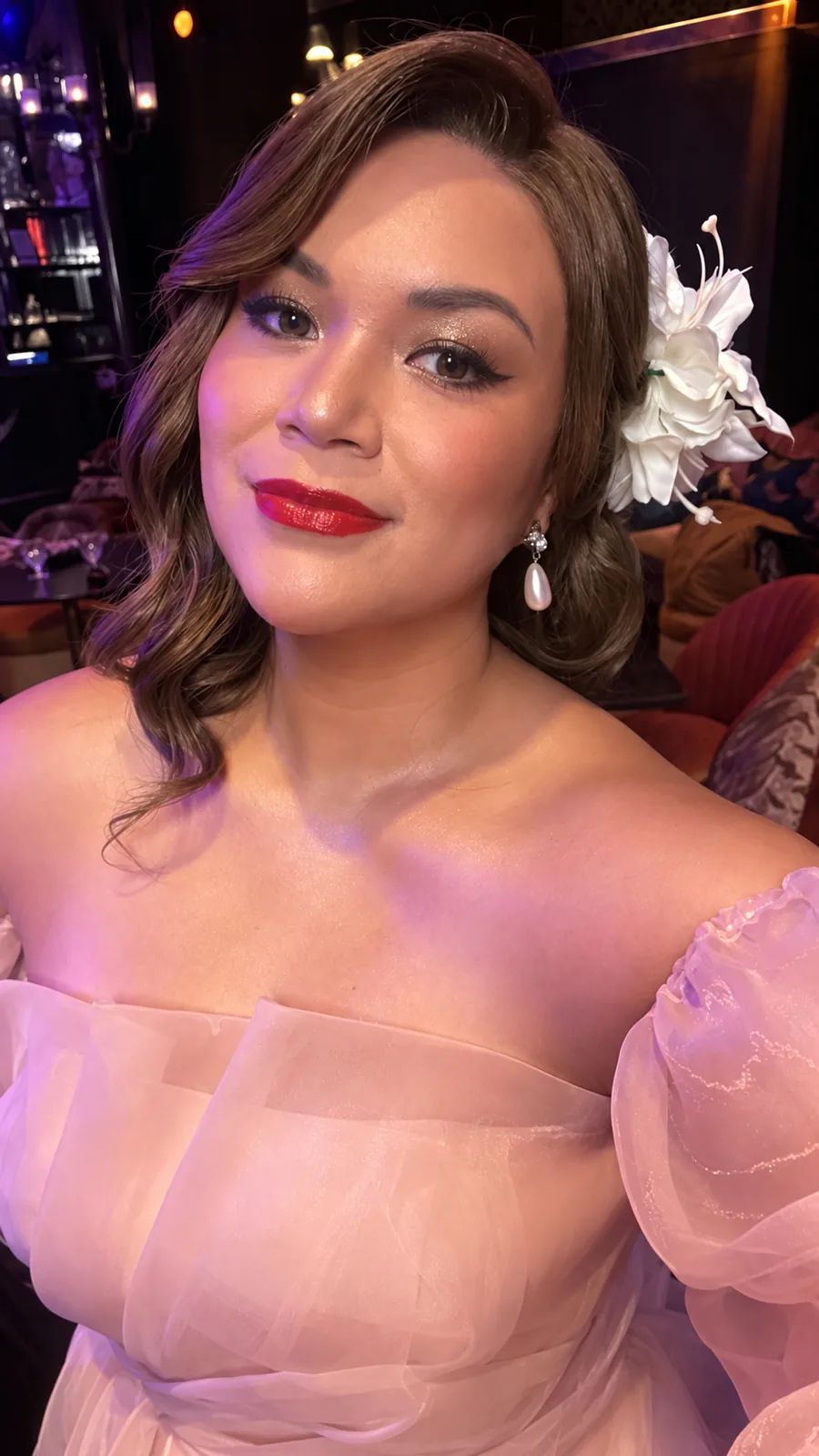 Evening look: curled brunette human-hair wig with a white flower and a pink tulle dress